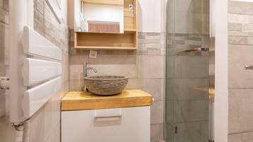 A modern bathroom with a stone sink, wooden countertop, and a glass shower enclosure.