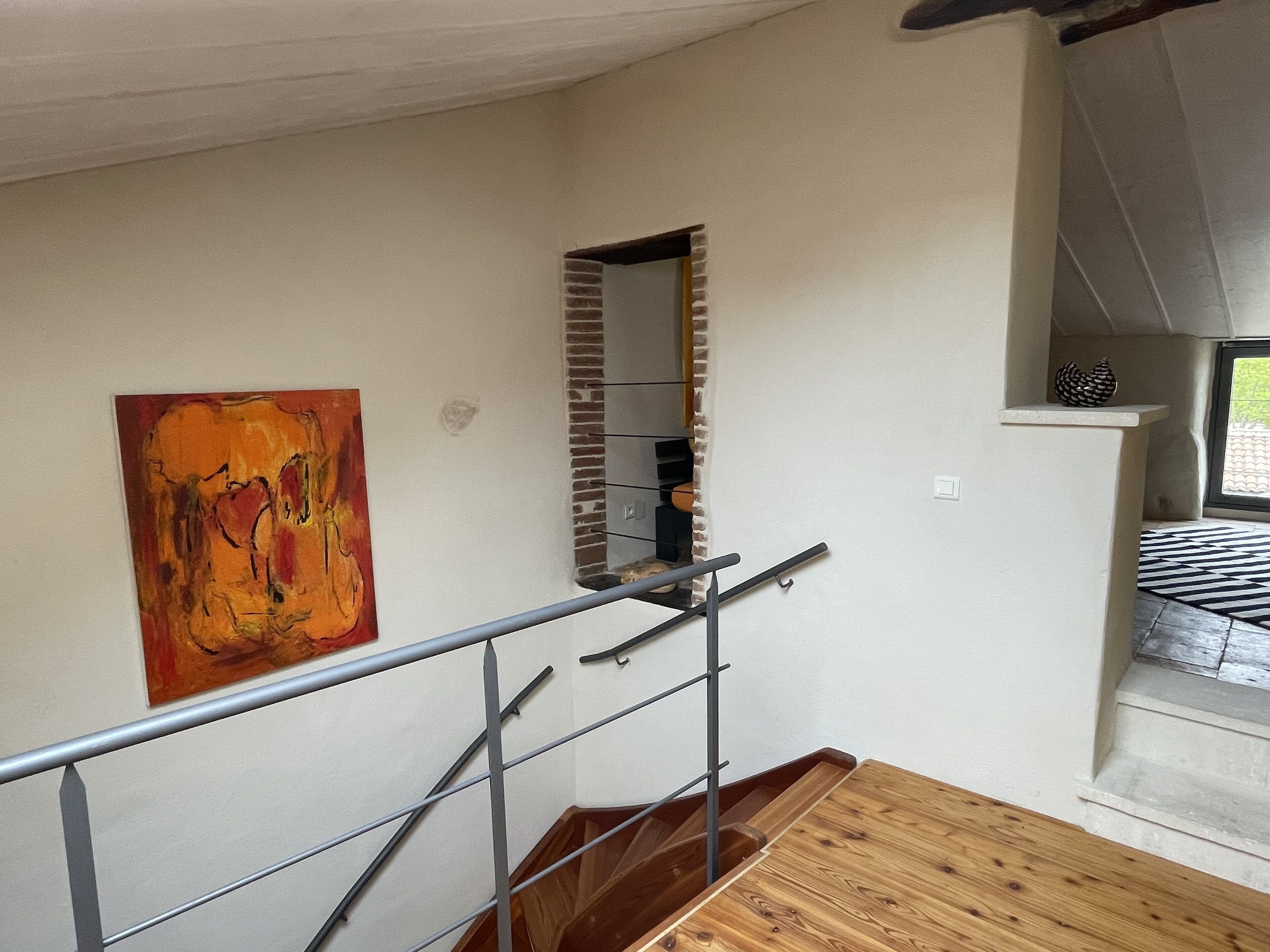 A staircase with a wooden finish, a metal handrail, and a brick wall with a small window.