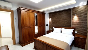 Une chambre avec une grande armoire en bois, un lit avec une literie blanche et une tête de lit en bois.