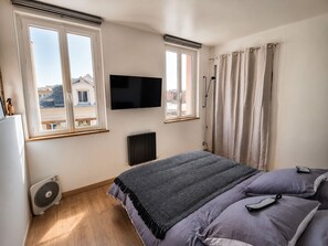 A bedroom with a bed, a TV, a radiator, and a window with curtains.