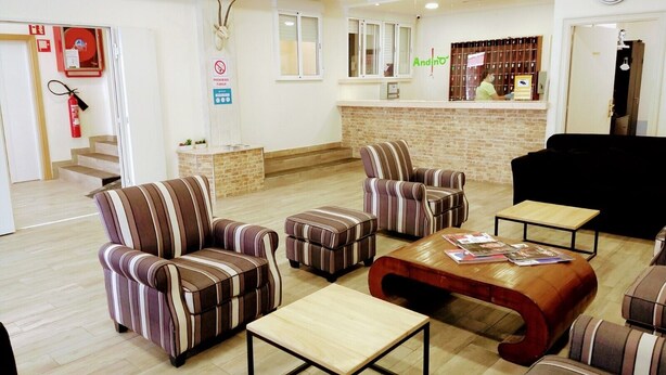 A hotel lobby with striped armchairs, a wooden coffee table, a reception desk, and a fire extinguisher. - Hotel Andino (Encamp)