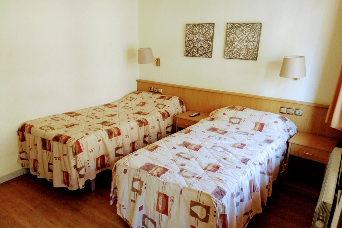 Habitación de hotel con dos camas individuales, cabecero de madera, mesitas de noche, lámparas y dos platos decorativos colgados en la pared.