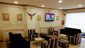 A lounge area with striped armchairs, a black sofa, a wooden coffee table, and a mounted TV displaying a sports event. - Hotel Andino (Encamp)