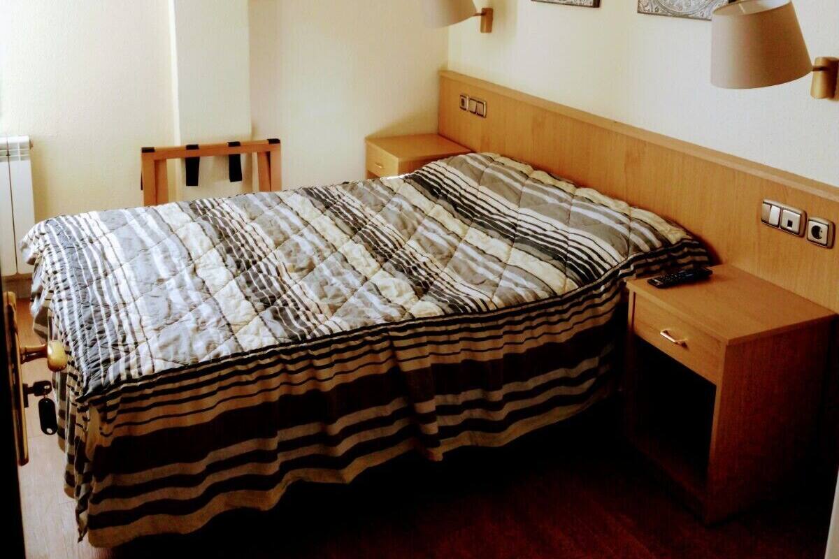 Una habitación de hotel con una cama de madera, una mesita de noche y dos lámparas fijadas a la pared.