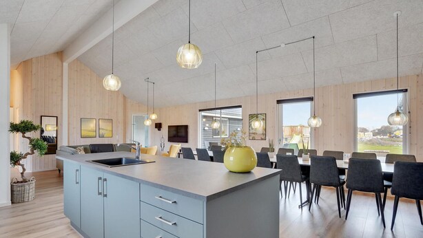 Cozinha moderna com ilha central, área de refeições com cadeiras e iluminação pendente.