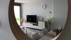 A modern living room with a flat-screen TV, a clock, and a dining area with a table and chairs.