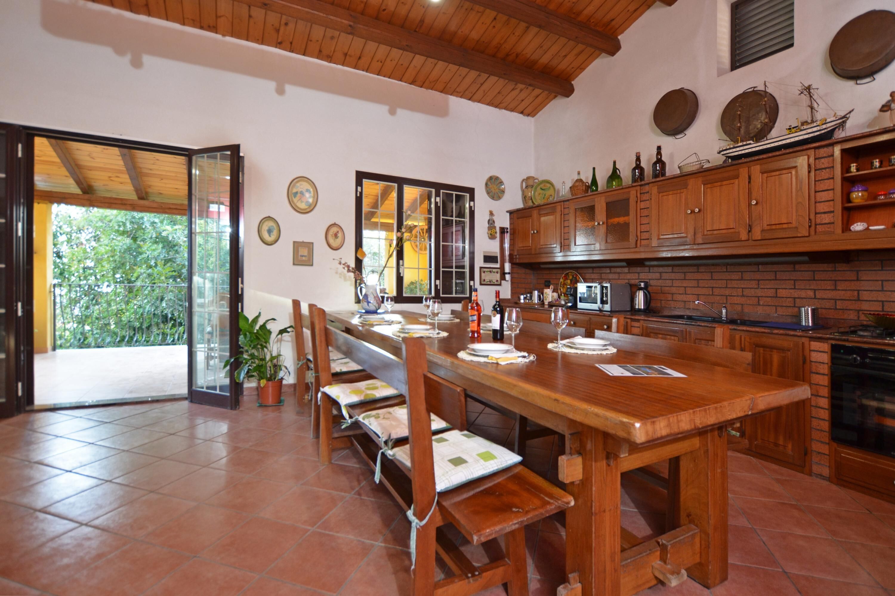 A spacious kitchen with a wooden table, benches, and a brick oven.