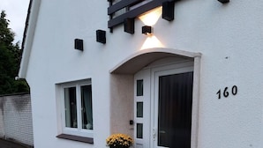Un bâtiment blanc avec le numéro « 160 » sur le côté droit, une porte et une fenêtre avec un jardon à l’avant.