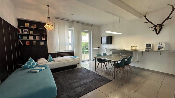 Una sala de estar moderna con un sofá, una mesa de comedor con sillas, una zona de cocina y un cráneo de ciervo montado en la pared.