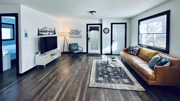 A modern living room with a wooden floor, a leather sofa, a TV, and a large window.
