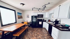A compact kitchen with white cabinets, a black refrigerator, a microwave, and a wooden dining table with benches.