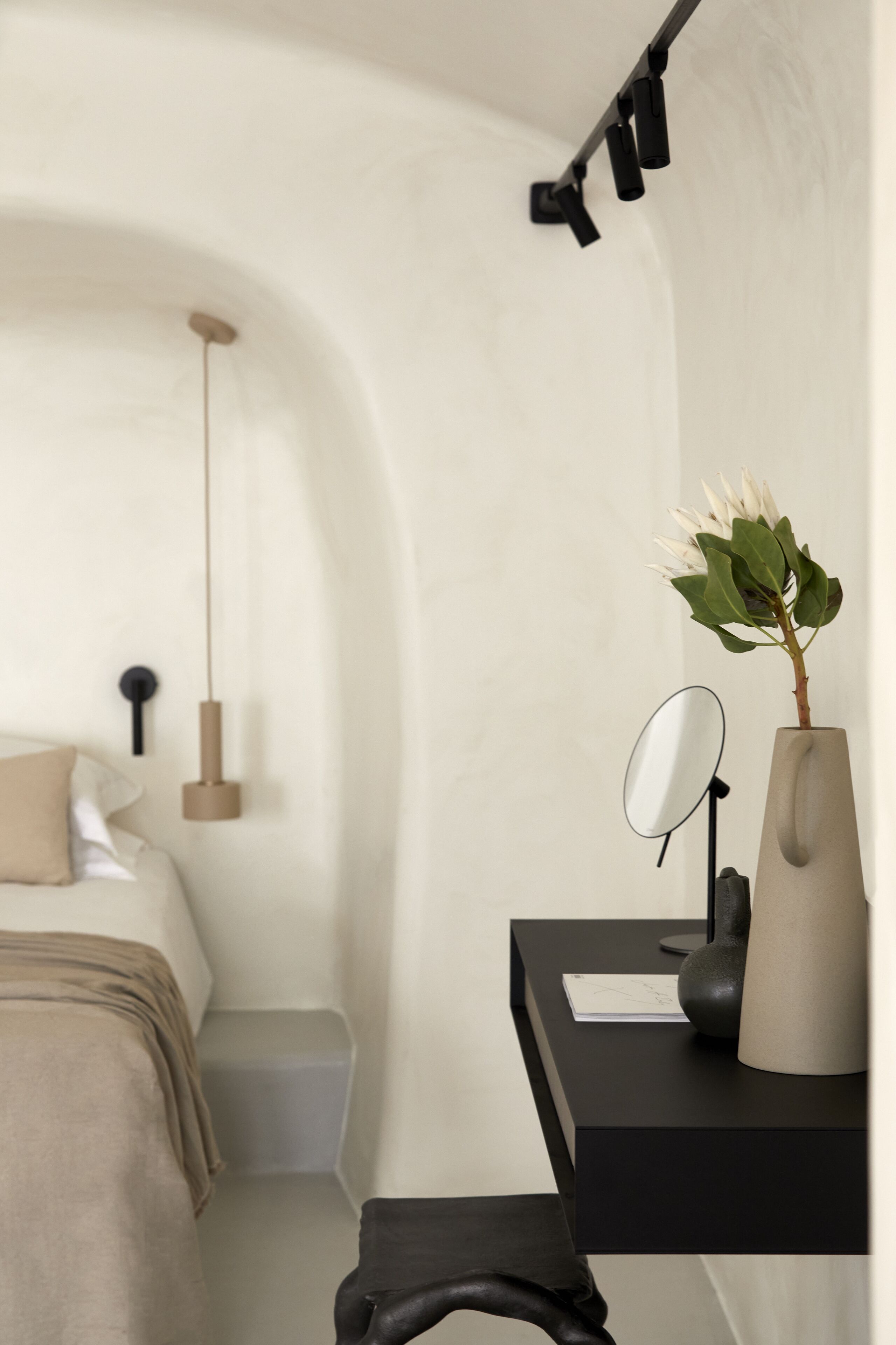 A modern bedroom with a bed, bedside table, and a desk with a mirror and vase.