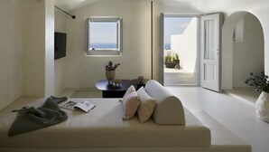 A minimalist room with a sofa, a small table, and a window overlooking a balcony. - Atoles Retreat (Santorini)