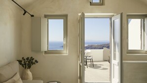 A room with a view of the sea, a sofa, a small table with a book, and a vase with flowers. - Atoles Retreat (Santorini)