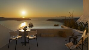 A terrace with a table and chairs overlooking a body of water during sunset. - Atoles Retreat (Santorini)