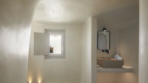 A modern bathroom with a bathtub, a window, and a built-in sink with a mirror. - Atoles Retreat (Santorini)