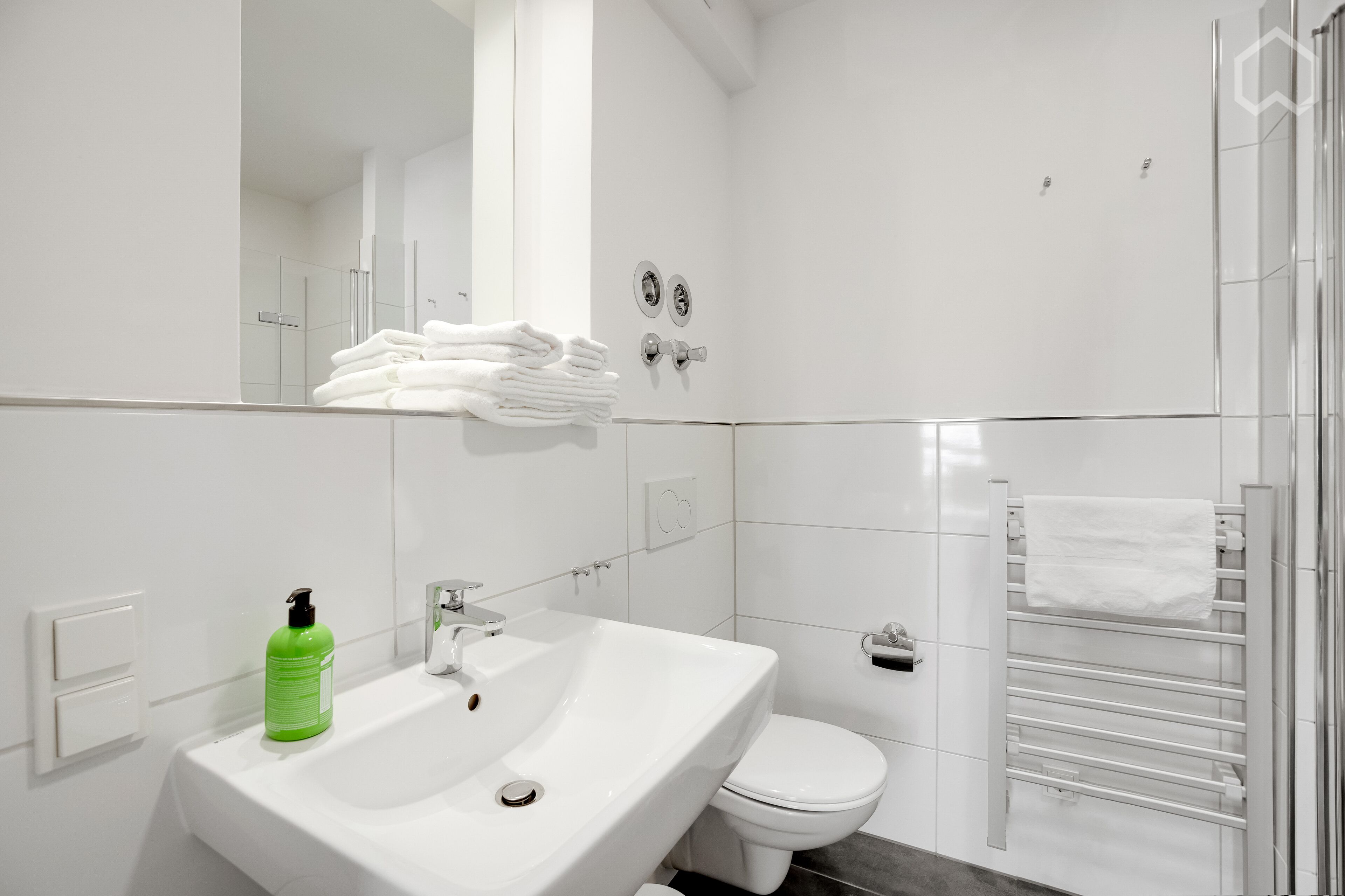 A modern bathroom with a white sink, green soap dispenser, and a towel rack.