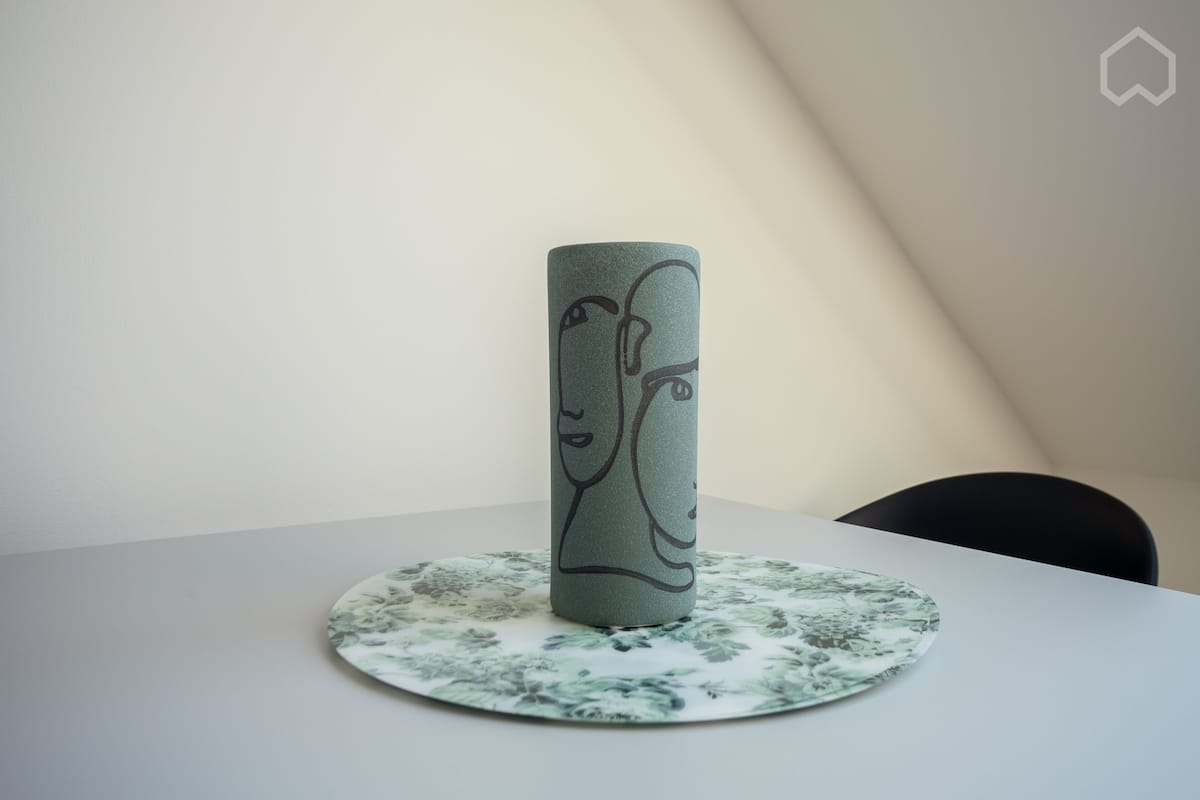 A cylindrical object with a face design on a table with a floral-patterned coaster.