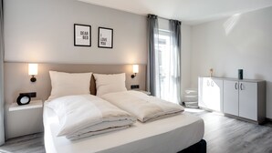 Quarto de hotel moderno com uma cama grande, duas mesas de cabeceira, um guarda-roupa e duas imagens emolduradas na parede.