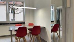 Een moderne eethoek met een tafel en rode stoelen, grote ramen en uitzicht op buiten.