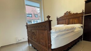 Een slaapkamer met een houten hemelbed, een raam met uitzicht op gebouwen en een betegelde vloer.