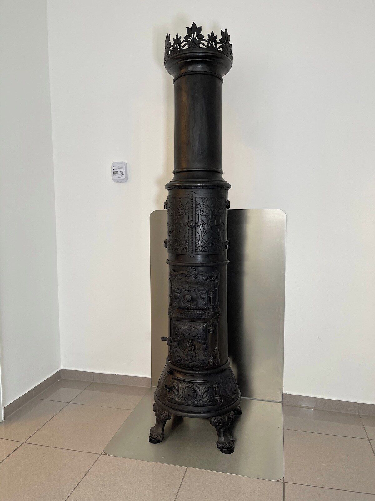Un alto e decorato fornello con motivi intricati, posizionato su un pavimento piastrellato davanti a una parete semplice.
