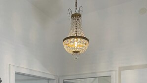 Een hal met witte wanden, een kroonluchter en een deur die leidt naar een kamer met een raam.