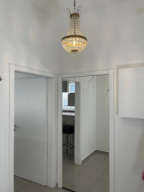 Ein Flur mit weißen Wänden, einer Chandelüster und einer Tür zu einem Zimmer mit einem Fenster.