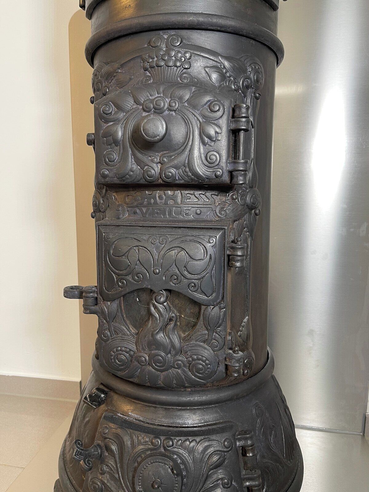 A vintage stove with intricate floral and scroll designs, a front door handle, and a small window.