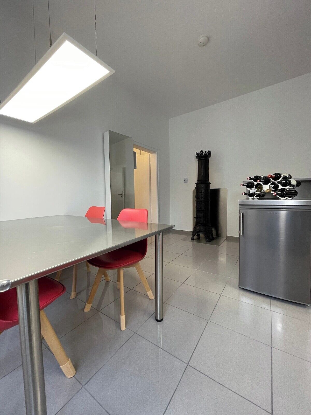 Uma cozinha moderna com geladeira de aço inoxidável, uma mesa de jantar com cadeiras vermelhas e um lustre.