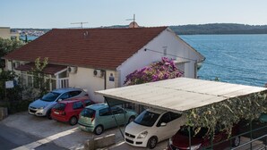 A coastal building with a red-tiled roof, a covered parking area, and a view of the sea. - A3 90m2 apt W.shared Pool & Balcony,next to Beach (Trogir)