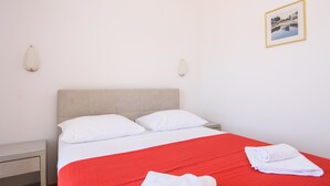 Et hotelværelse med en seng, to puder, et rødt sengetæppe, et natbord, et billede på væggen og et hvidt håndklæde på sengen.