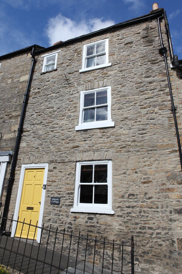 A stone building with three windows and a yellow door, labeled "Millgate Cottage."