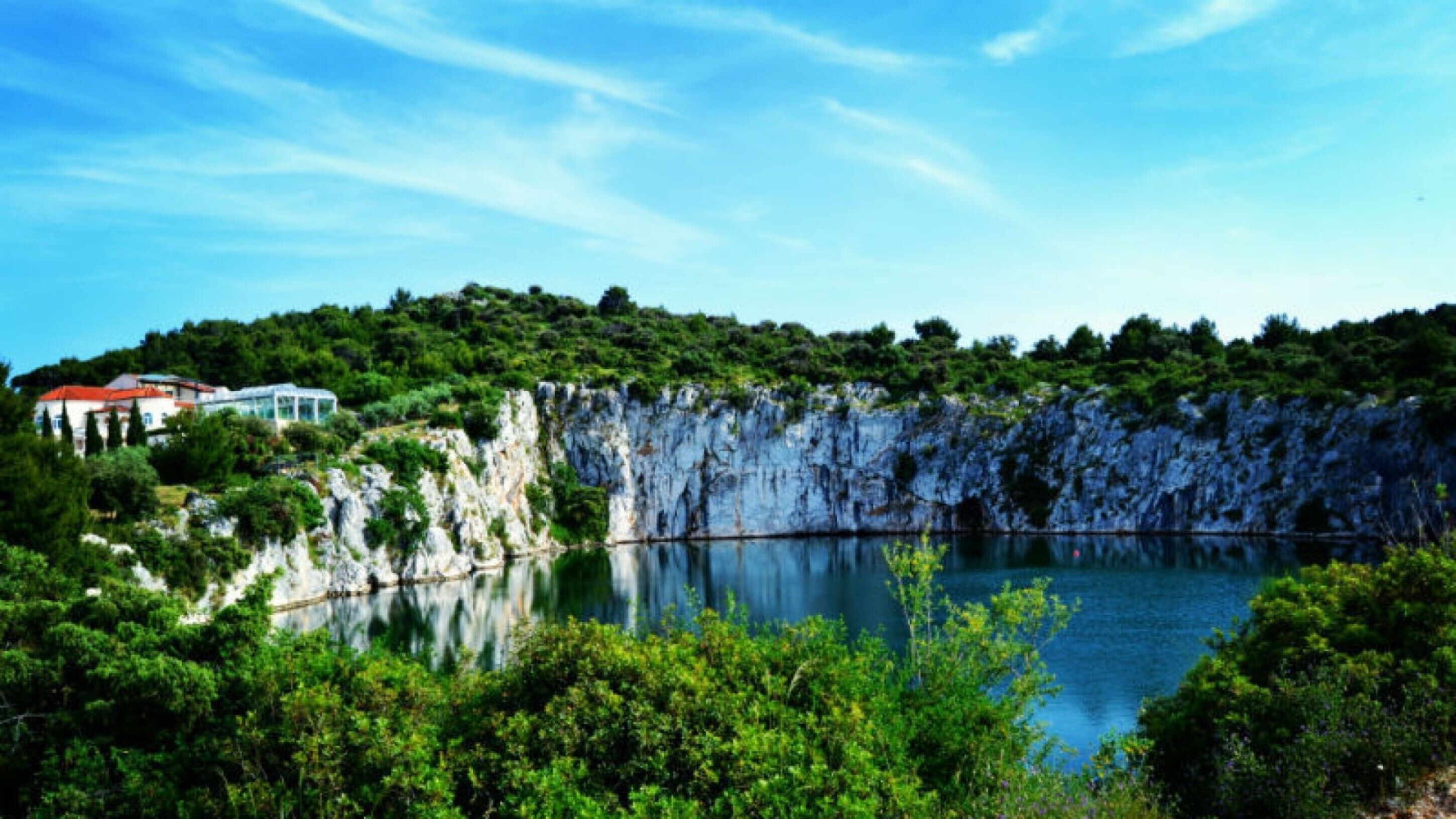 A coastal landscape with a clear lake, rocky cliffs, and a building with a red roof.