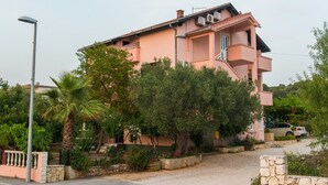 A pink multi-story residential building with balconies, surrounded by greenery and a gravel driveway. - A5 Cozy Apt. With big Garden, Balcony & Grill (Rogoznica)