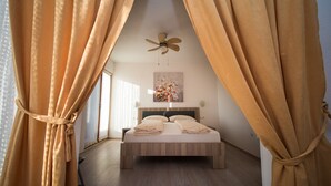 Une chambre à coucher avec un lit, des rideaux, un ventilateur de plafond et une œuvre d’art murale.