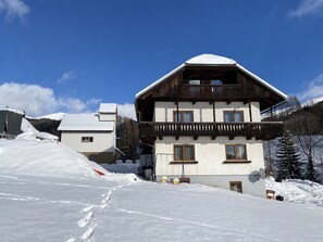 A chalet-style building with a sloped roof, wooden balconies, and a snow-covered landscape. - Nockalm Cottage Apartment Oswaldeck (Kärnten)