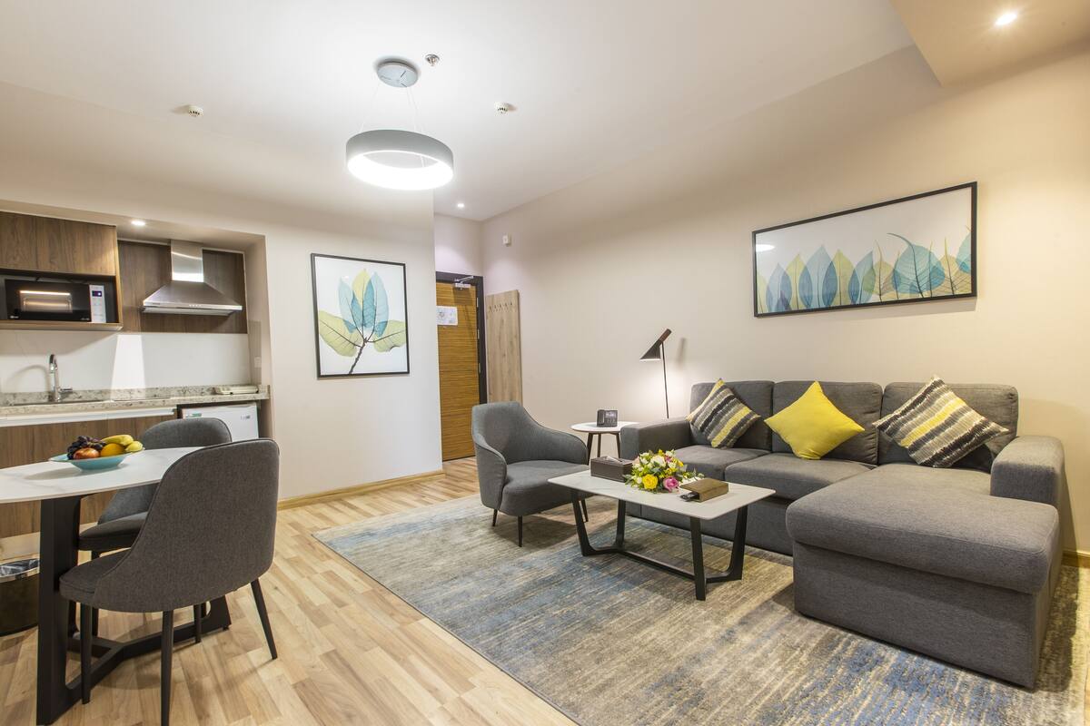 A modern living room with a grey sofa, a coffee table, and a dining area with a white table and chairs.