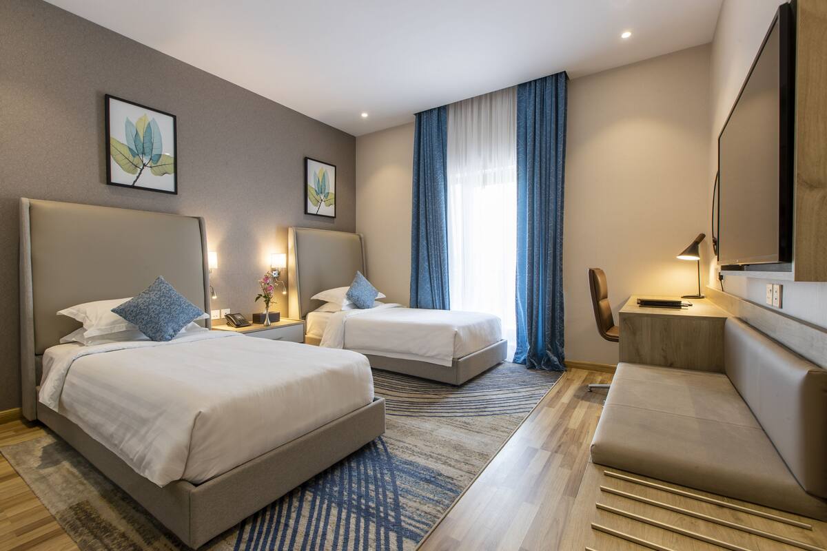 A hotel room with two beds, a sofa, a desk, and a large mirror.
