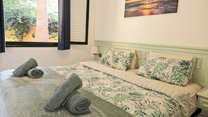 A neatly made bed with rolled towels, a painting of a sunset, and a window with curtains. - Vv Atlantic Garden with pool view, near beach (La Oliva)