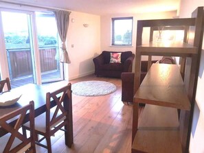 A living room with a wooden dining table, a sofa, and a large window with curtains.