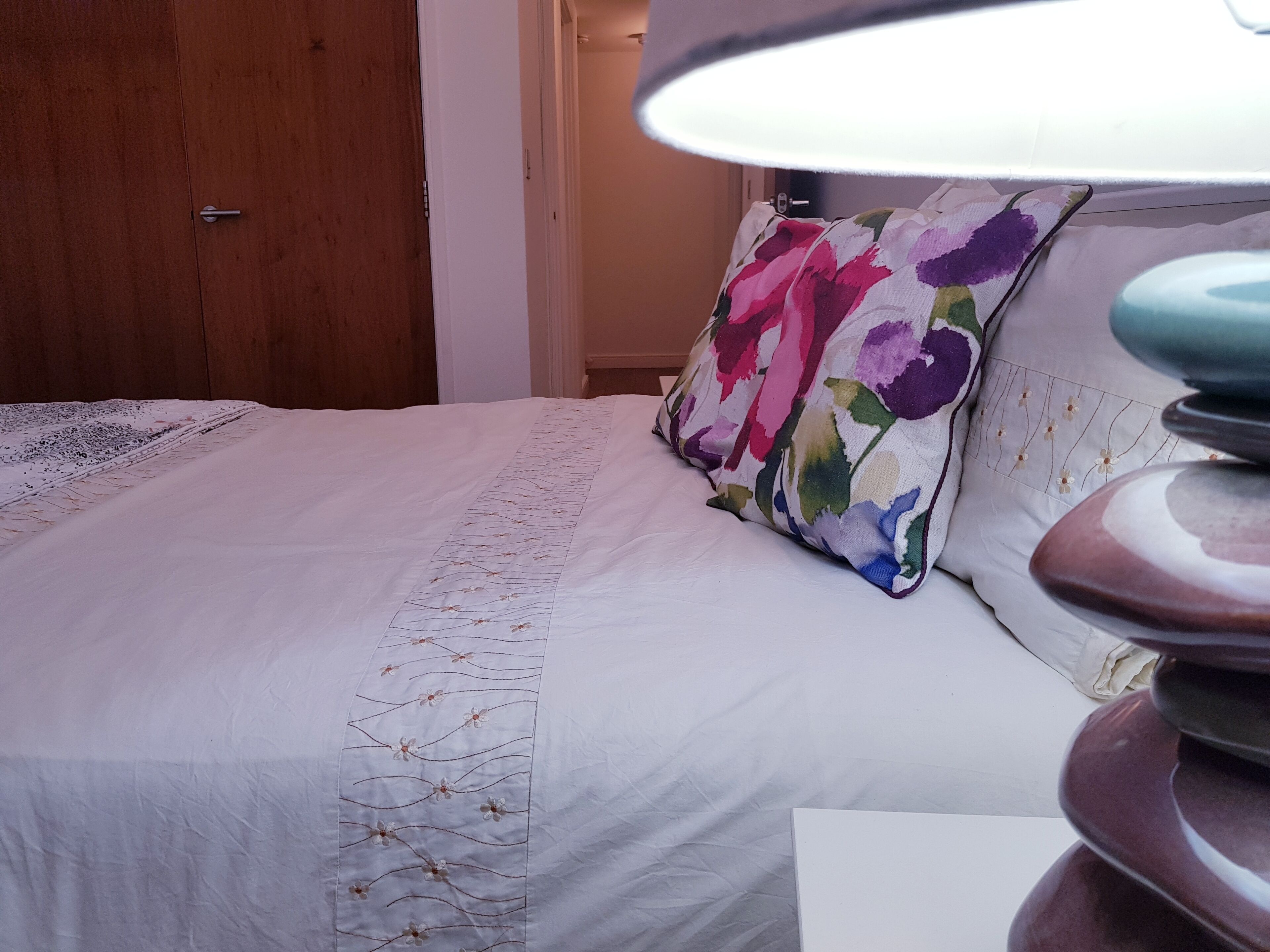 A neatly made bed with a floral pillow and a decorative headboard.