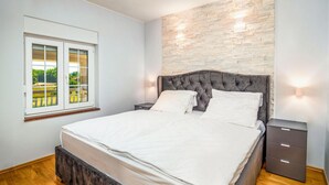 Un dormitorio con una cama grande, una mesita de noche, un aparador y una ventana con vistas a la vegetación.
