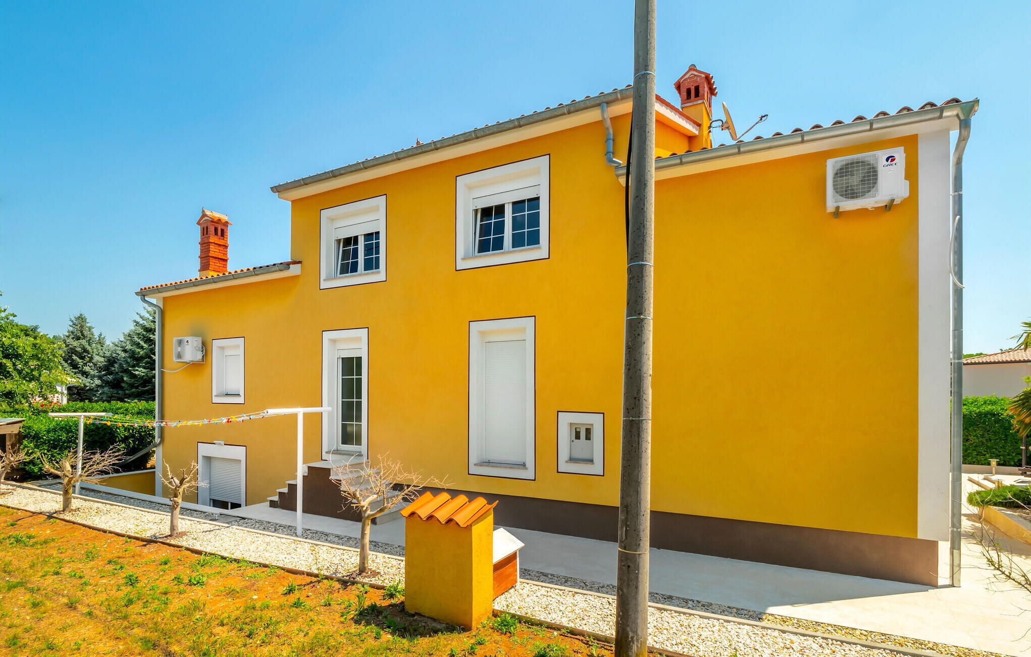 A yellow building with white windows and doors, a chimney, and a satellite dish.