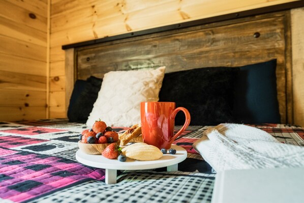 A cozy room with a wooden headboard, a quilted bedspread, and a small table with a plate of strawberries, blueberries, and cookies.