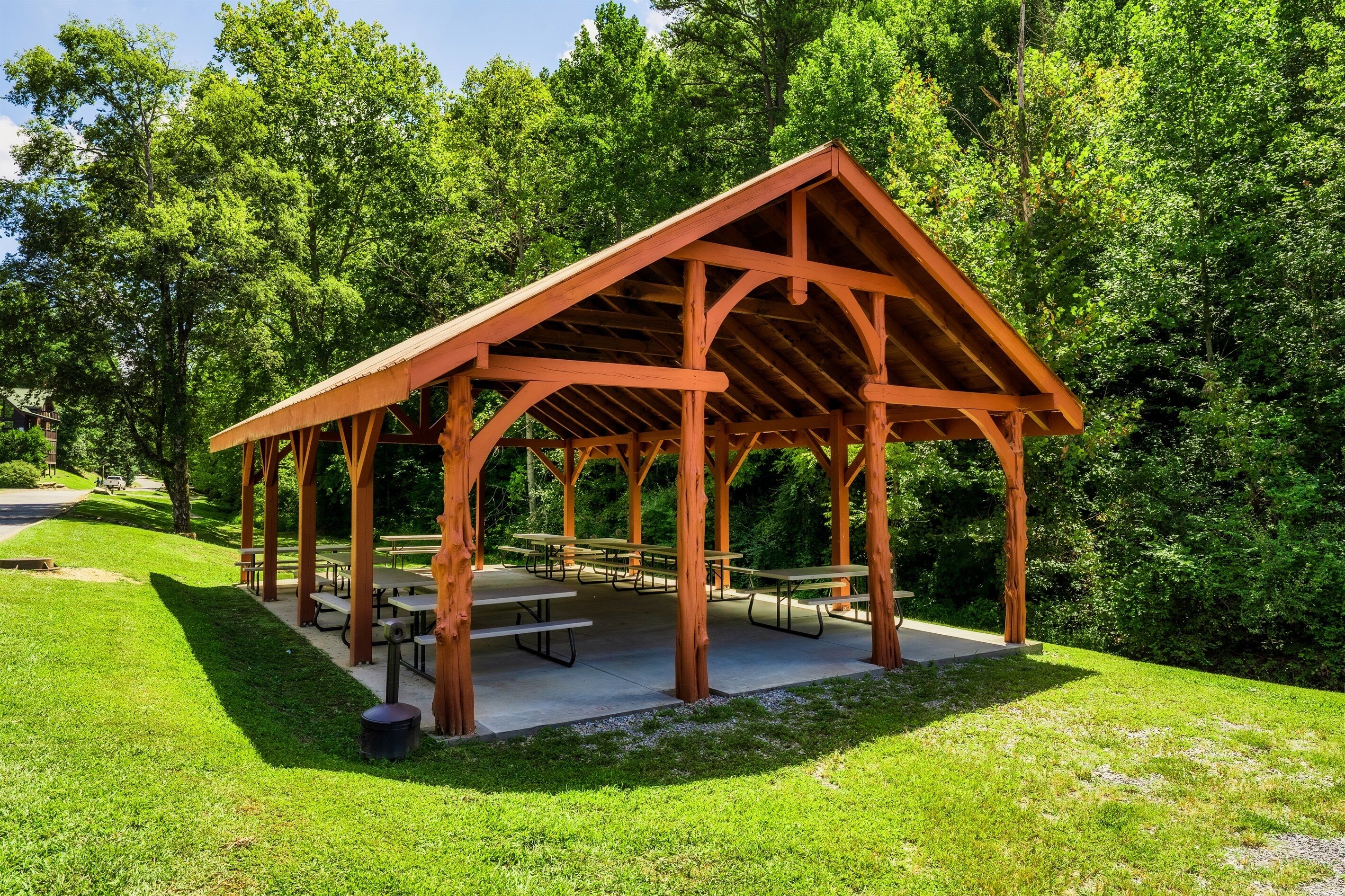 A wooden pavilion with picnic tables and benches, surrounded by lush greenery.