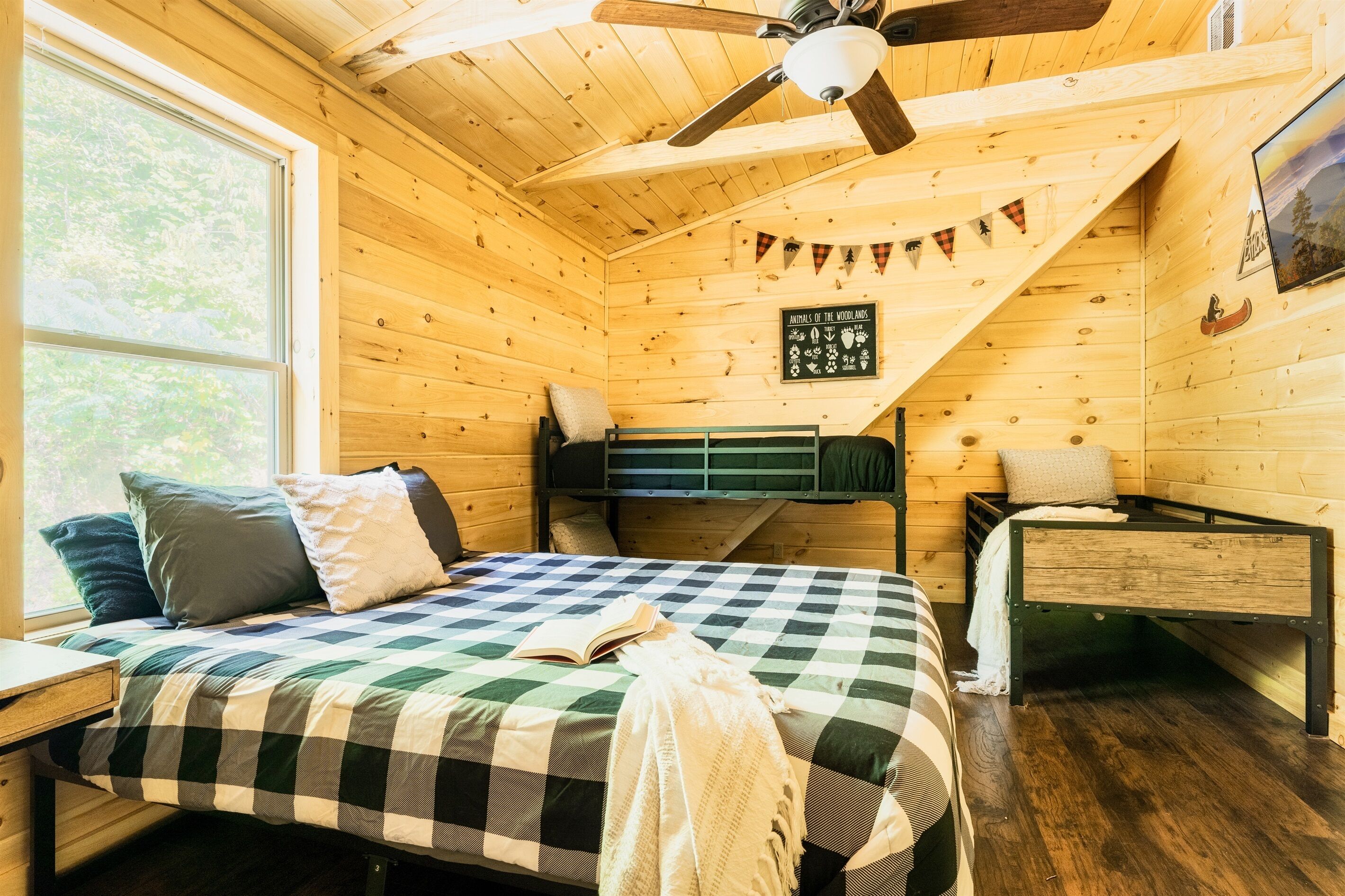 Een gezellig houten kamer met een bed, een bureau, een stoel, een stapelbed en een plafondventilator.