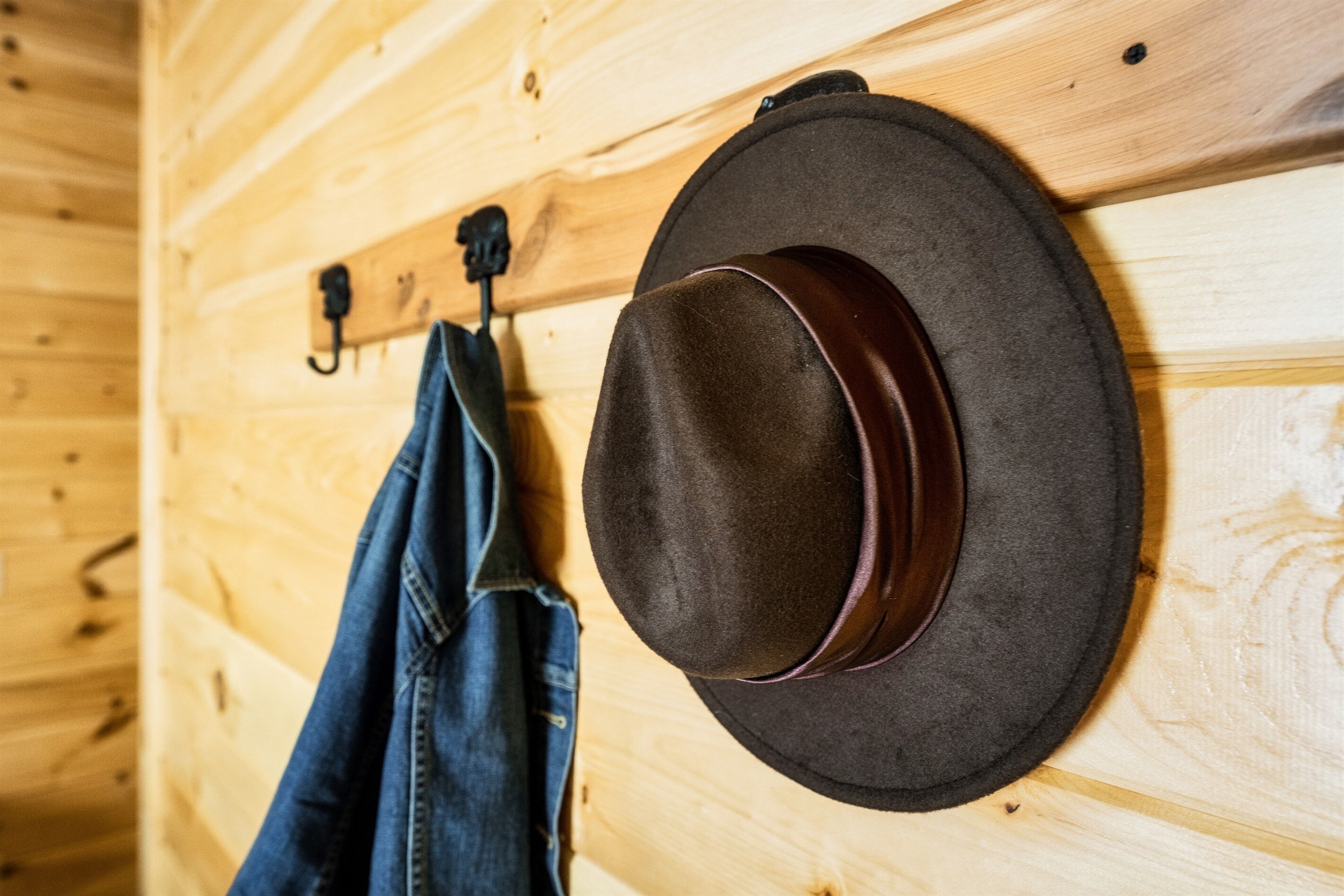 A wooden wall with a hat and a pair of jeans hanging on hooks.