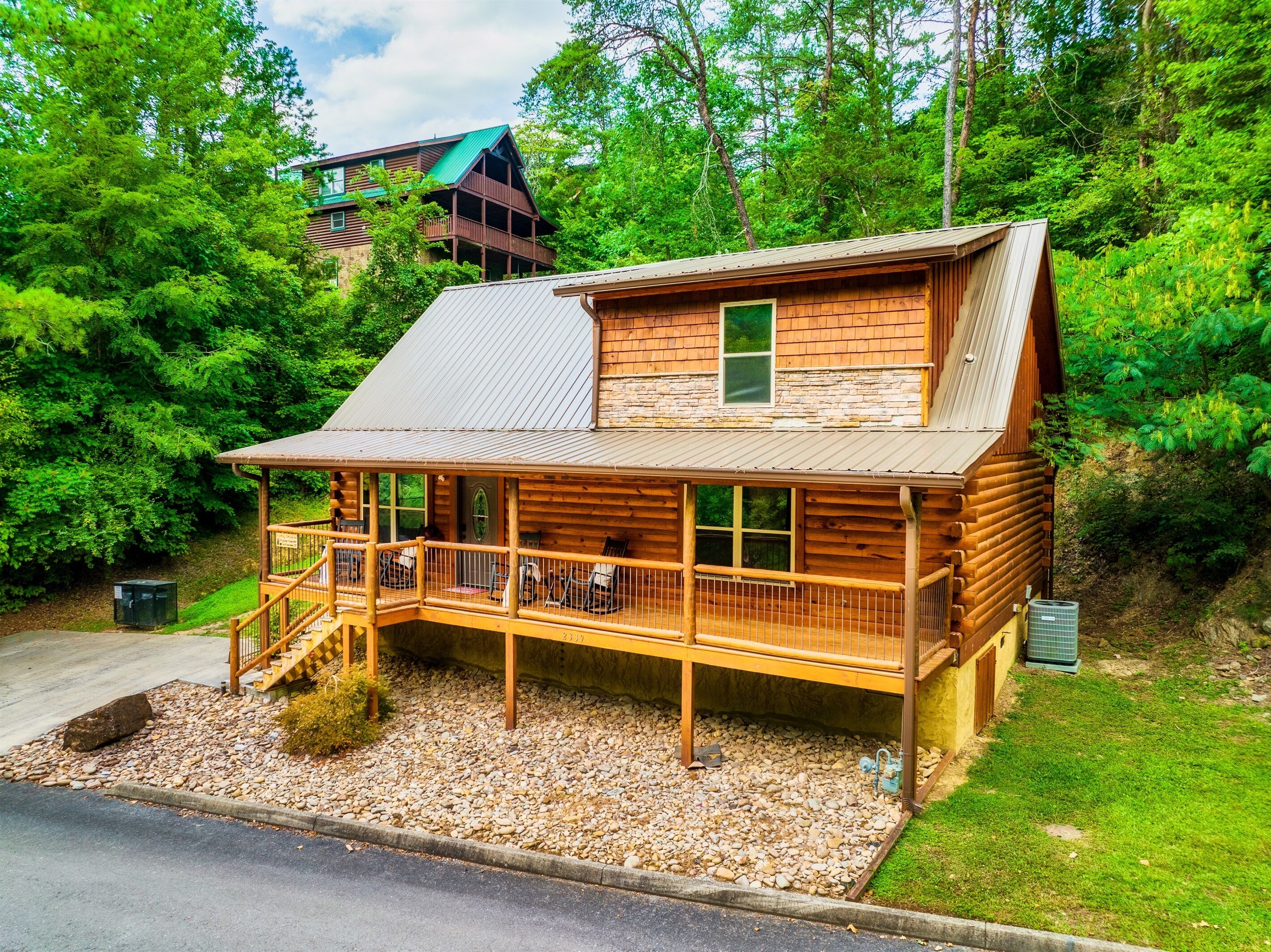 A log cabin with a wooden deck, stone foundation, and a metal roof.