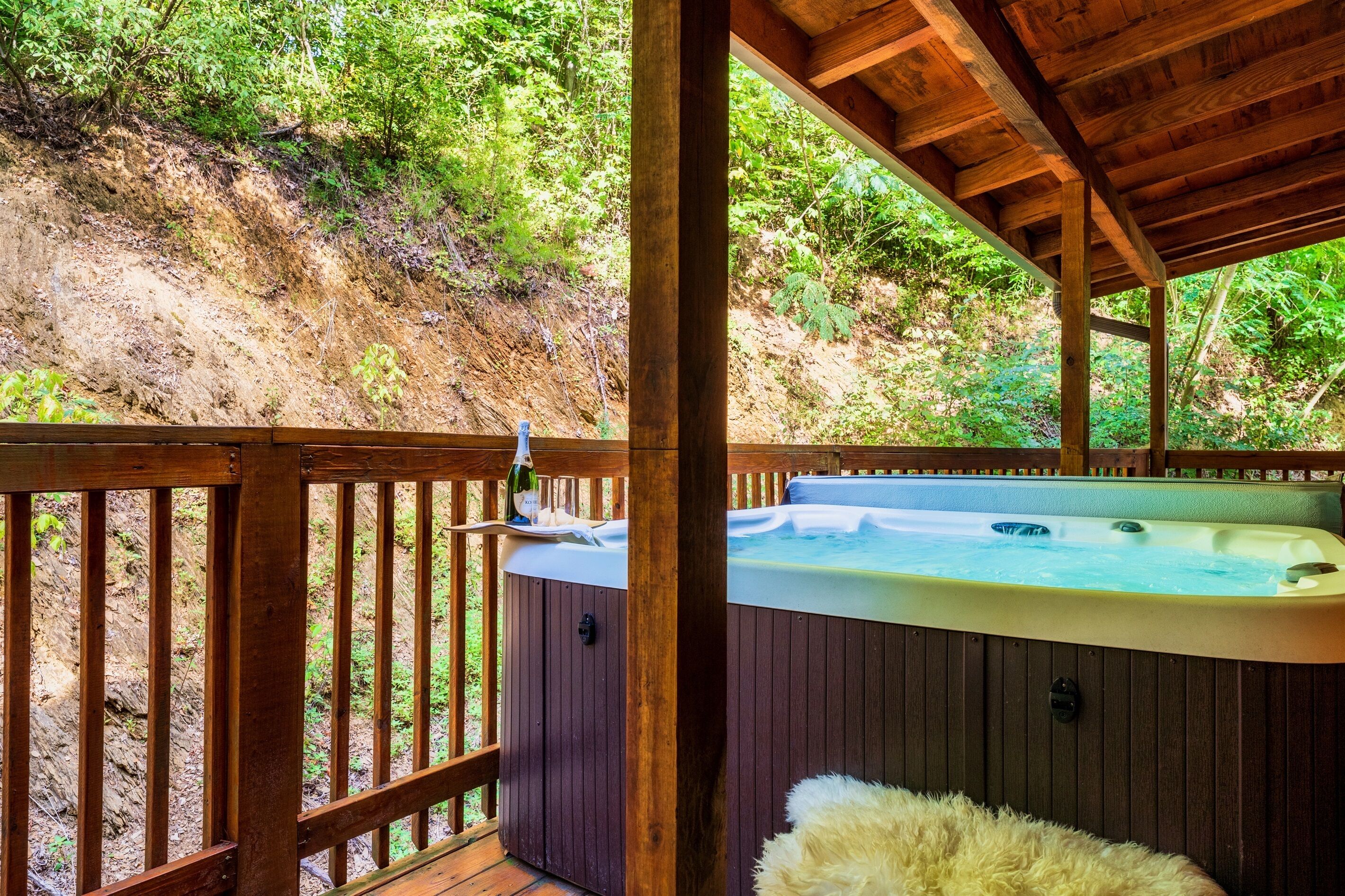 Un jacuzzi bajo una terraza de madera con vista a una ladera boscosa.